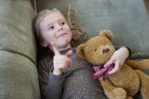 Young girl lying on sofa with her teddy bear — Stock Photo