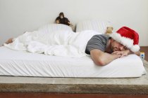 Чоловік середнього віку в капелюсі Санта спить у ліжку — стокове фото