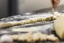 Chef sprinkling flour on gnocchi in commercial kitchen, close-up partial view — Stock Photo