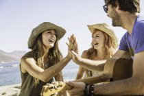 Mid adult friends playing guitar and high fiving at coast, Cape Town, South Africa — Stock Photo