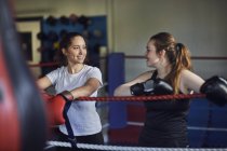 Young female boxers leaning against boxing ring ropes chatting — Stock Photo