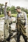 Man and woman standing in river wearing waders holding fishing rod smiling — Stock Photo