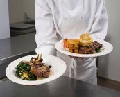 Шеф-кухар тримає дві тарілки м'яса з овочами — стокове фото