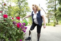 Середня доросла жінка з протезною ногою, в саду, поливні рослини — стокове фото