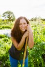 Porträt einer jungen Frau, die sich in Schrebergarten an Gartengerät lehnt — Stockfoto