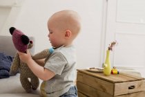 Дитяча дівчинка вказує грати з плюшевим ведмедем у вітальні — стокове фото