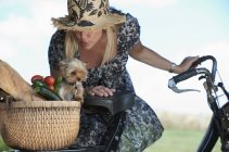Donna matura su bici elettrica con cane e verdure nel cestino — Foto stock