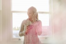 Young woman on phonecall, holding hot drink — Stock Photo