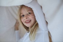 Girl playing under blanket looking at camera — Stock Photo