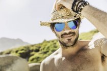 Retrato del hombre con gafas de sol de espejo azul y sombrero de paja en la playa, Ciudad del Cabo, Sudáfrica - foto de stock