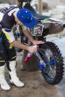 Junger männlicher Motocross-Teilnehmer lehnt sich nach vorne und putzt Motorrad — Stockfoto