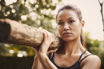Portrait of woman training,  lifting tree trunk on shoulder in park — Stock Photo
