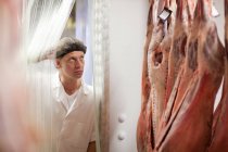 Carniceiro masculino olhando para a carne no congelador — Fotografia de Stock