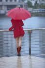 Giovane donna in rosso in attesa sul lungomare — Foto stock
