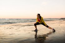 Läuferin dehnt sich am Strand — Stockfoto