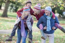 Familie zusammen im Park, Mutter und Vater tragen Kinder lachend auf dem Rücken — Stockfoto