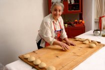 Older woman rolling dough on board — Stock Photo