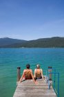 Вид сзади пары, сидящей на пирсе у озера — стоковое фото