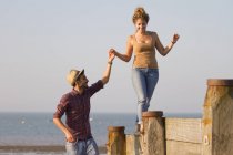 Junge Frau balanciert auf Groynes und hält Mann die Hand — Stockfoto