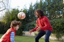 Батько і син грають з футболом в саду посміхаючись — стокове фото