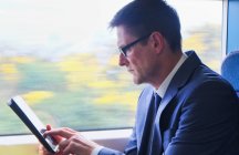 Зрілий бізнесмен сидить у потязі, використовуючи цифровий планшет — стокове фото