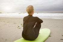Female surfer sitting on surfboard looking out from Rockaway Beach, New York, USA — Stock Photo