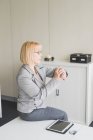 Зрелая деловая женщина сидит на рабочем столе и смотрит на наручные часы — стоковое фото