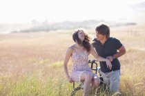 Couple playing on bicycle in tall grass — Stock Photo
