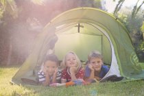 Портрет троих детей, лежащих в садовой палатке — стоковое фото