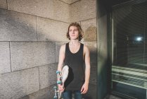 Retrato de jovem homem skatista urbano de pé segurando skate — Fotografia de Stock
