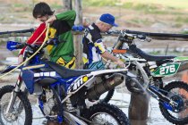 Two male motocross competitors cleaning motorcycles with water hoses — Stock Photo