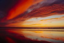 Vista de la playa húmeda que refleja la puesta del sol cielo naranja - foto de stock