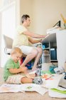 Отец за компьютером, пока маленький сын играет на полу — стоковое фото