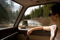 Mujer mirando por la ventana del coche en el paisaje del bosque - foto de stock