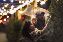 Romántico feliz pareja disfrutando de la ciudad durante las vacaciones de invierno mirando a los árboles de Navidad - foto de stock