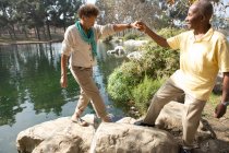 Portrait of senior couple stepping on rocks by lake in park — Stock Photo