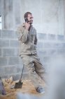 Чоловік стоїть з лопатою, розмовляючи на мобільному телефоні — стокове фото