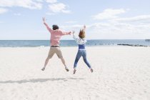 Rear view of couple jumping mid air on beach — Stock Photo