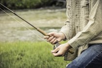 Cropped view of young man winding fishing reel on fishing rod — Stock Photo