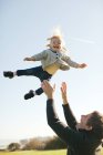 Kleinkind von Vater gegen blauen Himmel geschleudert — Stockfoto
