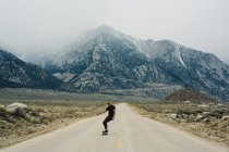 Homem de skate na estrada por montanhas, Lone Pine, Califórnia, EUA — Fotografia de Stock