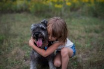 Маленька дівчинка обіймає собаку на трав'яному полі — стокове фото