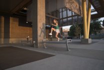 Молодая женщина прыгает через скамейку в городской среде — стоковое фото