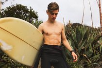Молодий чоловік йде до пляжу, несучи дошку для серфінгу — стокове фото