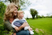 Mother and daughter sitting in field, looking away — Stock Photo