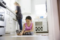 Девушка сидит на полу кухни и рисует — стоковое фото