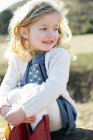 Menina loira bonito sentado no log abraçando joelhos — Fotografia de Stock