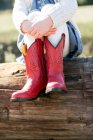 Neck down view of girl sitting on log wearing red cowboy boots — Stock Photo