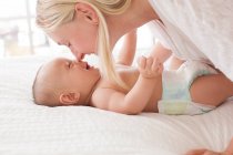 Femme adulte moyenne nez à nez avec bébé fils couché sur le lit — Photo de stock