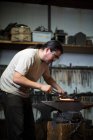 Male metalsmith shaping red hot metal on workshop anvil — Stock Photo